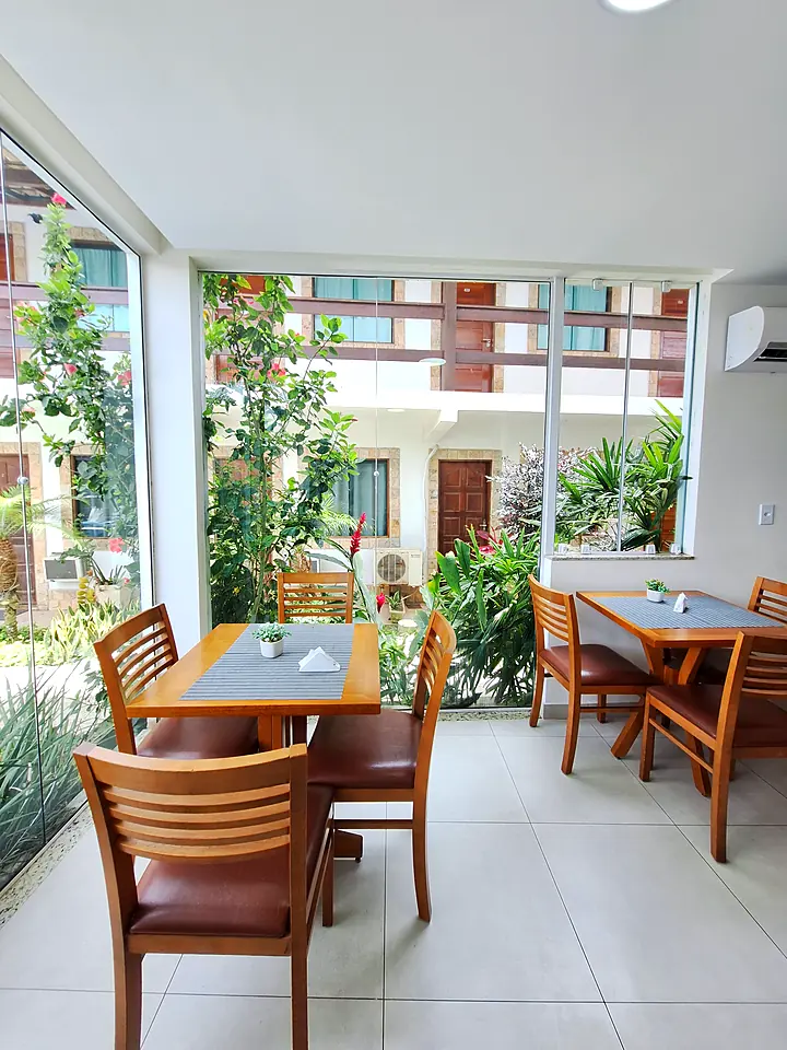 Salão do café da manhã com mesas de madeira e jardim ao fundo